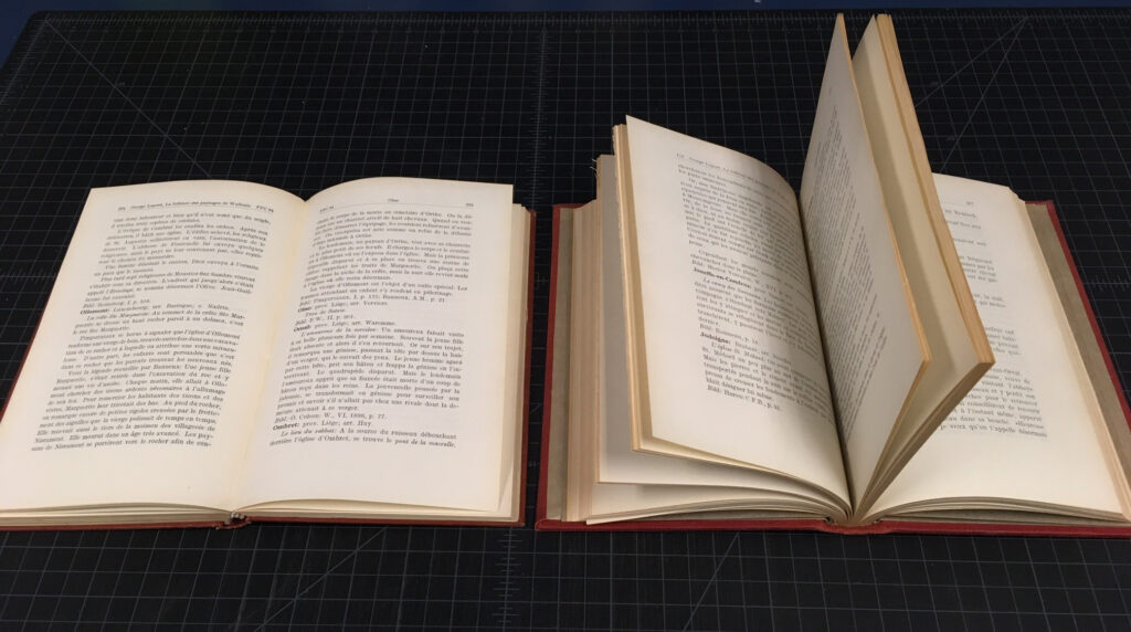 Two copies of the same book opened on a table. The one at left opens flat, the one at right must be held open.