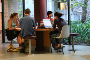 4 students sit at a library table using laptops