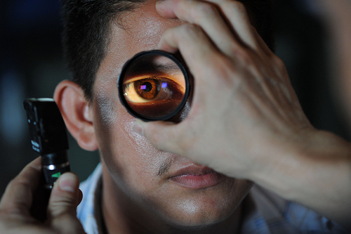 Image 1: Photo of man’s eye being magnified, with another person’s hand holding the magnifying tool