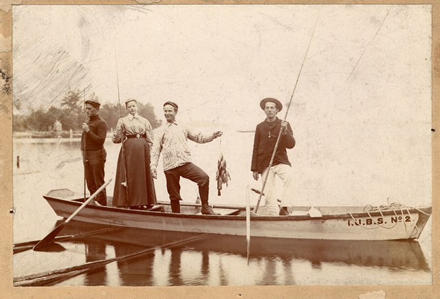  Sepia-toned photograph of a woman and three men in a fishing boat. 