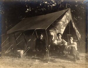  Black and white photograph of three young men posing outside a tent. 