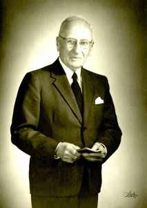  Black and white photograph of a man in a suit with glasses.