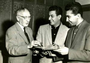  Black and white photograph of a professor and students examining a book. 