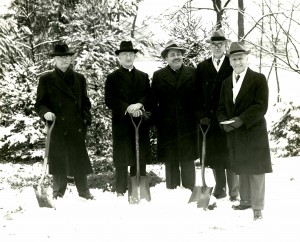  Black and white photograph of men in suits and winter coats with shovels in the snow. 