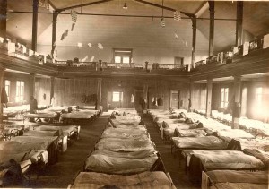  Black and white photograph of hospital beds lined up in rows in a large room. 