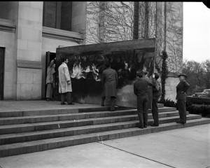  Black and white photograph of workers bringing a large mural panel into a building. 