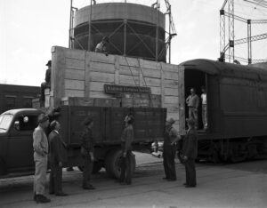  Black and white photograph of workers unloading a large crate from a truck. 