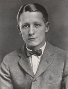  Black and white image of a young man in a suit and bowtie. 