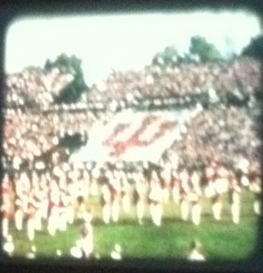 Still image from a color film showing a crowd at a football game. 