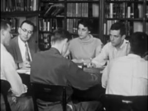  Still image of students and a teacher around a table in discussion. 