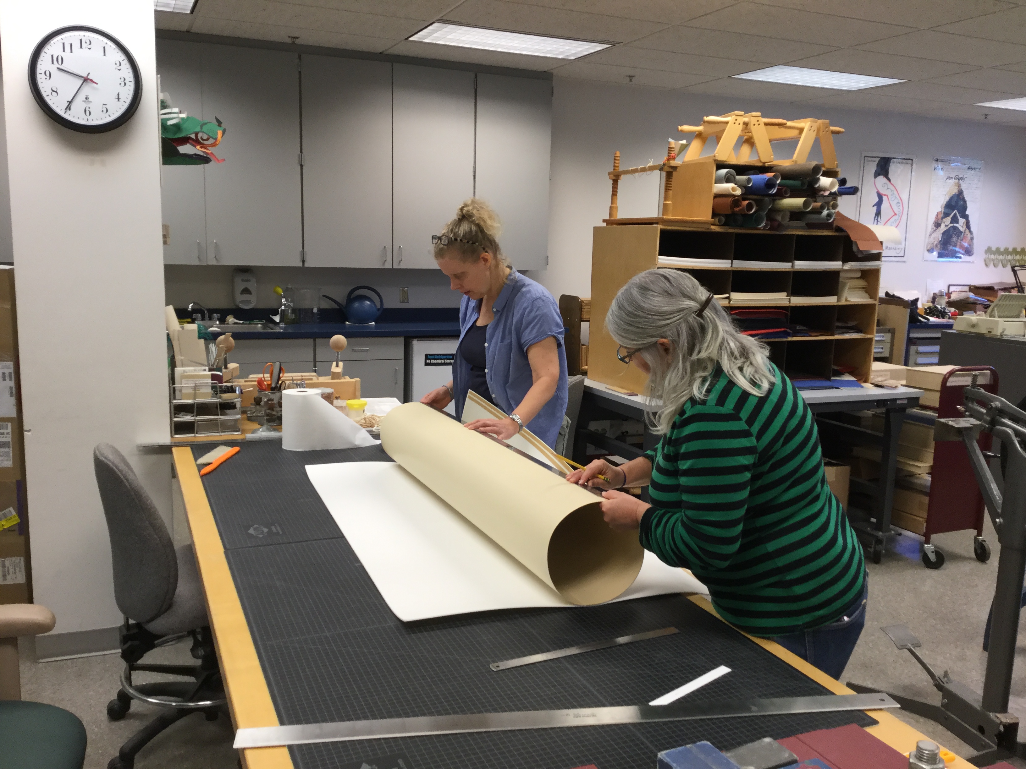 Two conservation technicians making a large tube from a large sheet of board