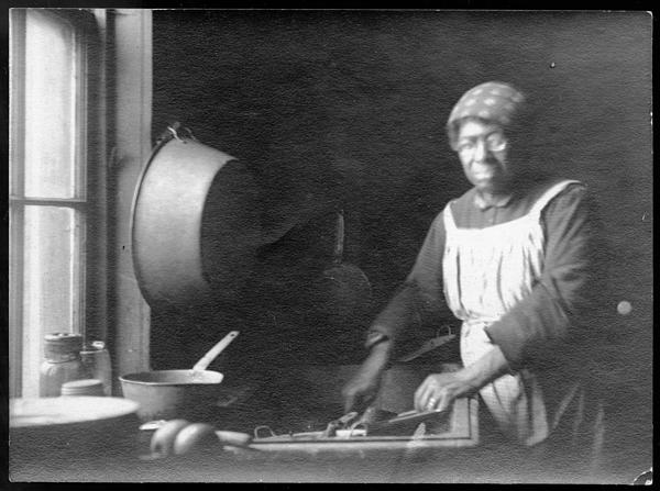 Black and white image of a women in an apron working in a kitchen.