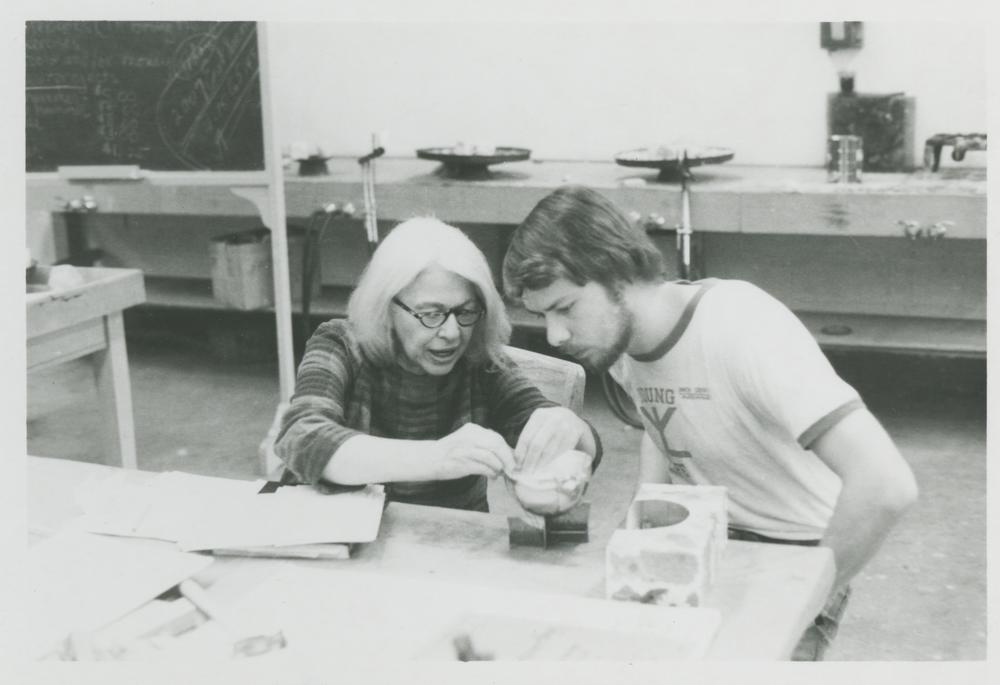 Black and white photograph of Alma Eikerman and a student seated side-by-side at a work table. Eikerman is demonstrating a technique for the student. 