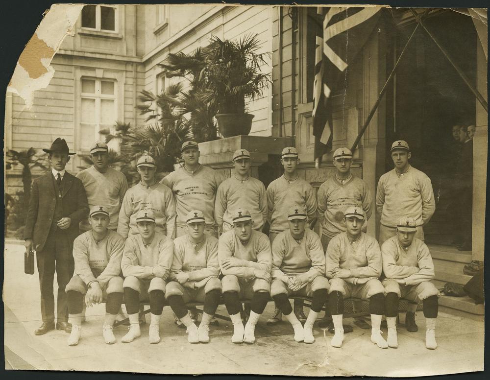 Black and white photograph of 14 members of the IU baseball team and their coach in front of their hotel