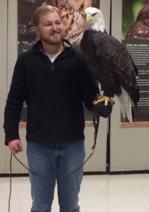 Color photograph of Will Schaust with a bald eagle perched on his arm. 