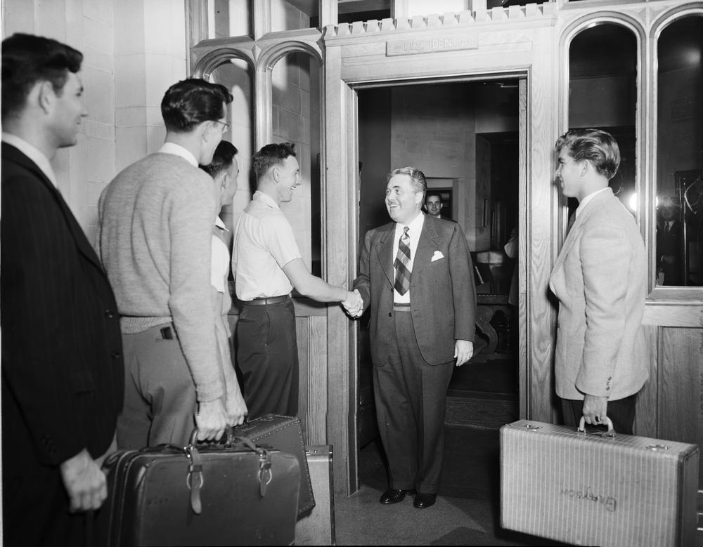 Black and white photograph of President Herman Wells greeting students with suitcases in hand at the entrance to Bryan Hall. 