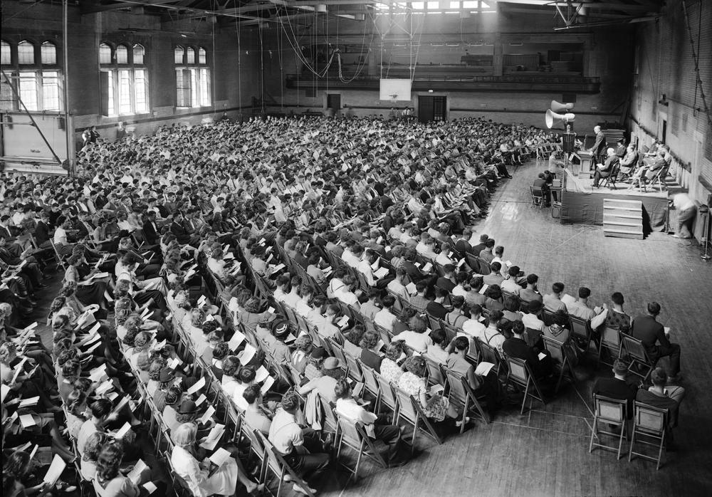 Black and white photograph of Freshman convocation - a large crowd of seated students surrounds a central stage. 