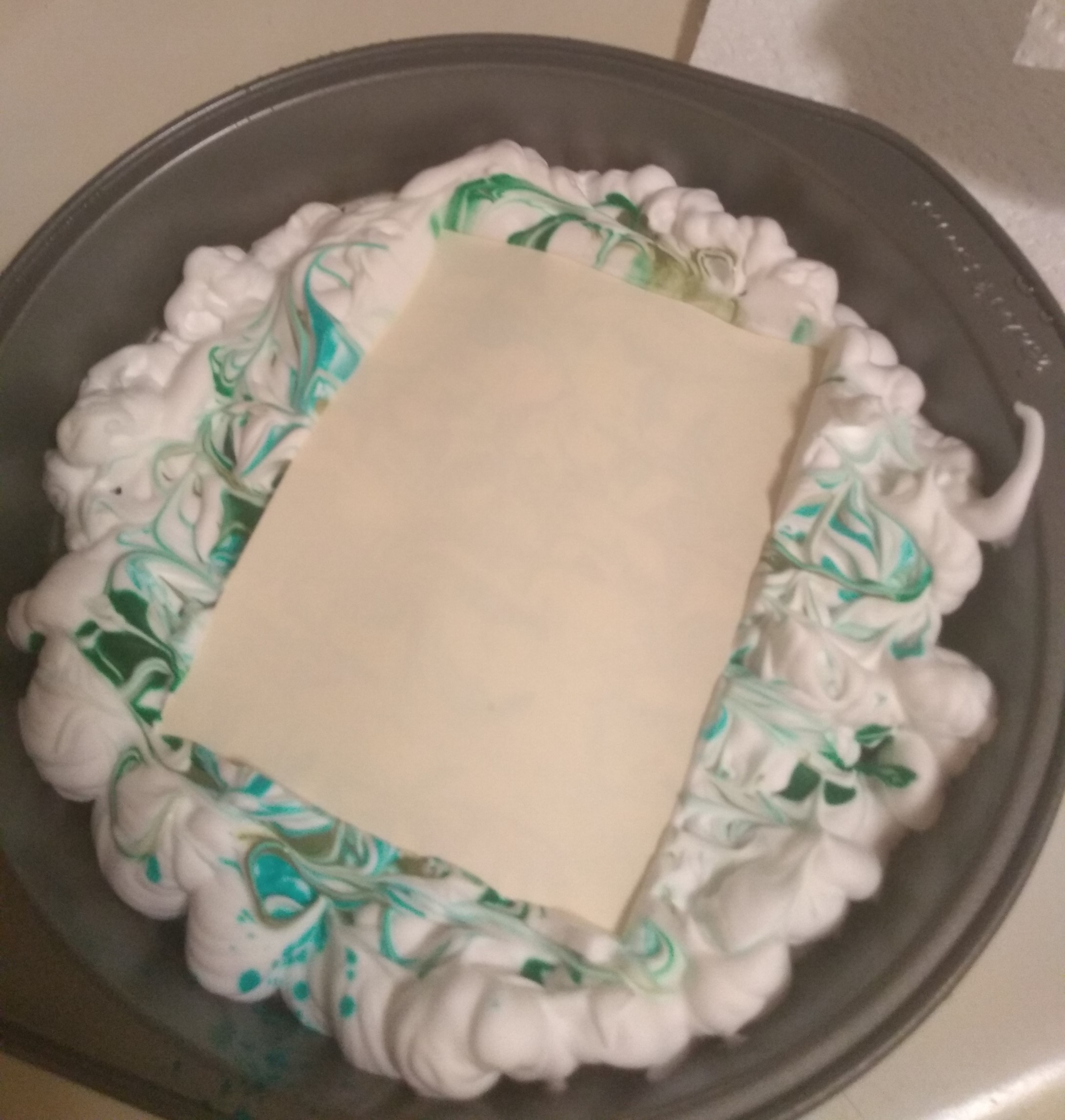 A piece of paper sits in a tray of dyed shaving cream