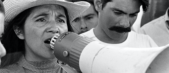 still image of Dolores Huerta speaking into a megaphone from the documentary, Dolores.