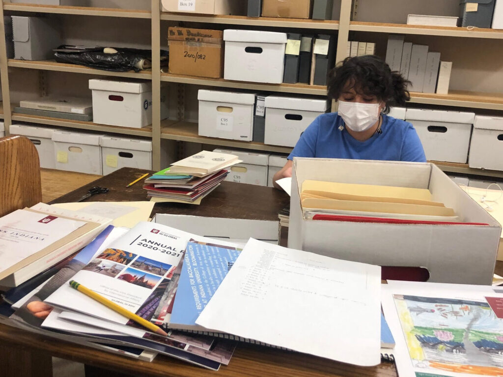Photo of author Maya Cazares sitting behind a pile of loose archival materials