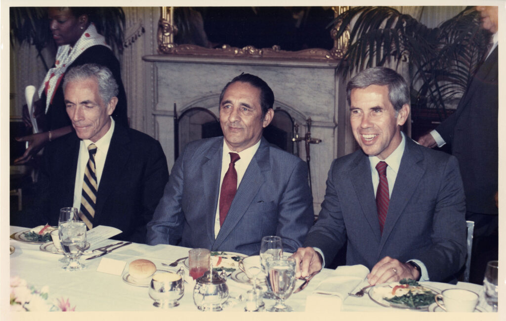 U.S. Senate photograph of Senator Claiborne Pell (D-RI), President of El Salvador Jose Napoleon Duarte, and Senator Richard Lugar (R-IN), May 6, 1984. The men are seated at a table with plates of food and drinks in front of them.