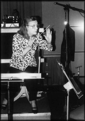 Black and white photograph of composer Angela Morley in action, waving a composer's baton.