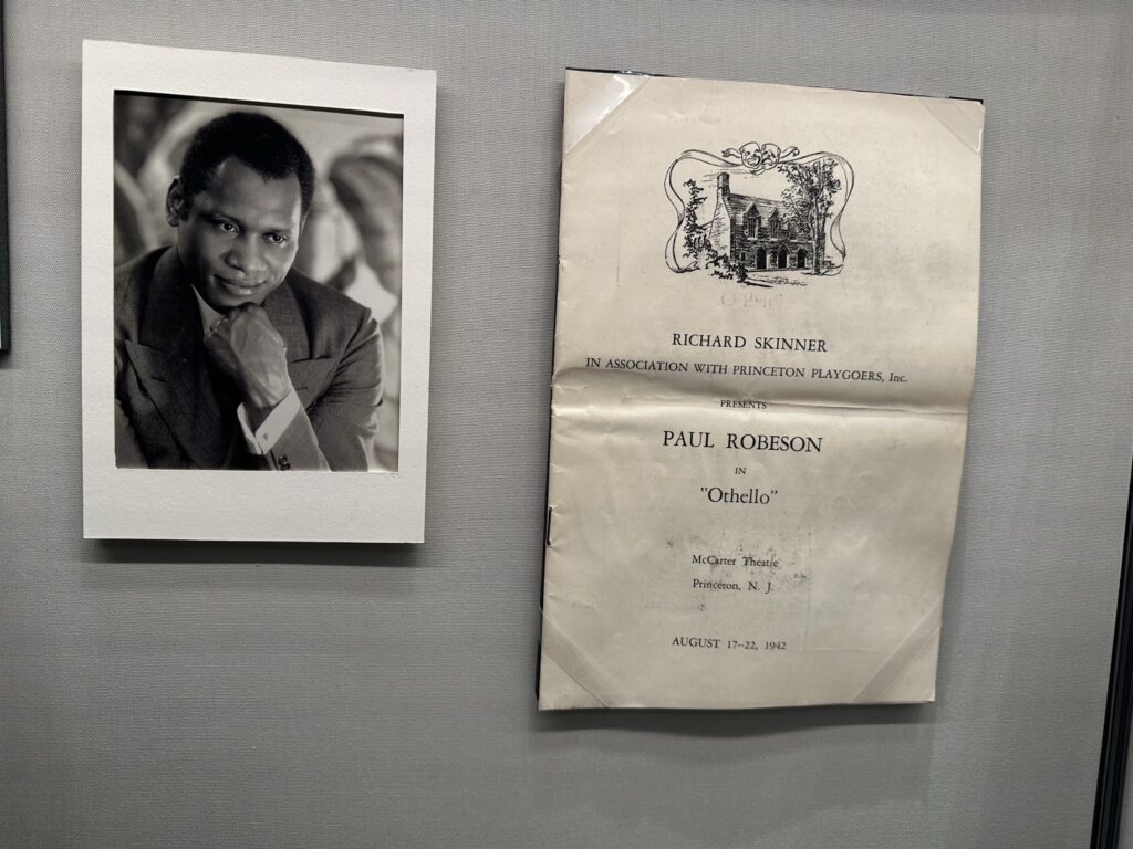 A photo of Paul Robeson. He is smiling slightly and has his chin resting lightly on his hand. Beside the photo is the program for the 1942 performance.