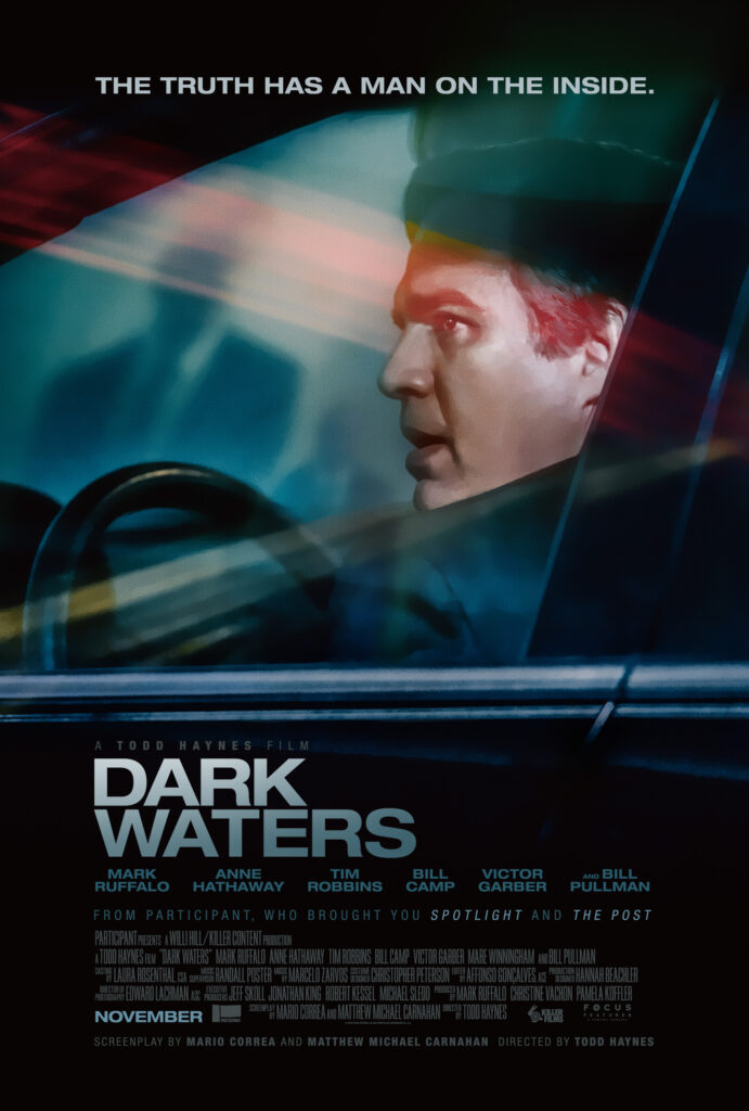 A movie poster for "Dark Waters", depicting Mark Ruffalo through his car window as ne nervously glances over his shoulder. A bright red lighn illuminates his eyes. An ominous suited figure appears as a reflection in the mirror. Above them is the words "THE TRUTH HAS A MAN ON THE INSIDE".
