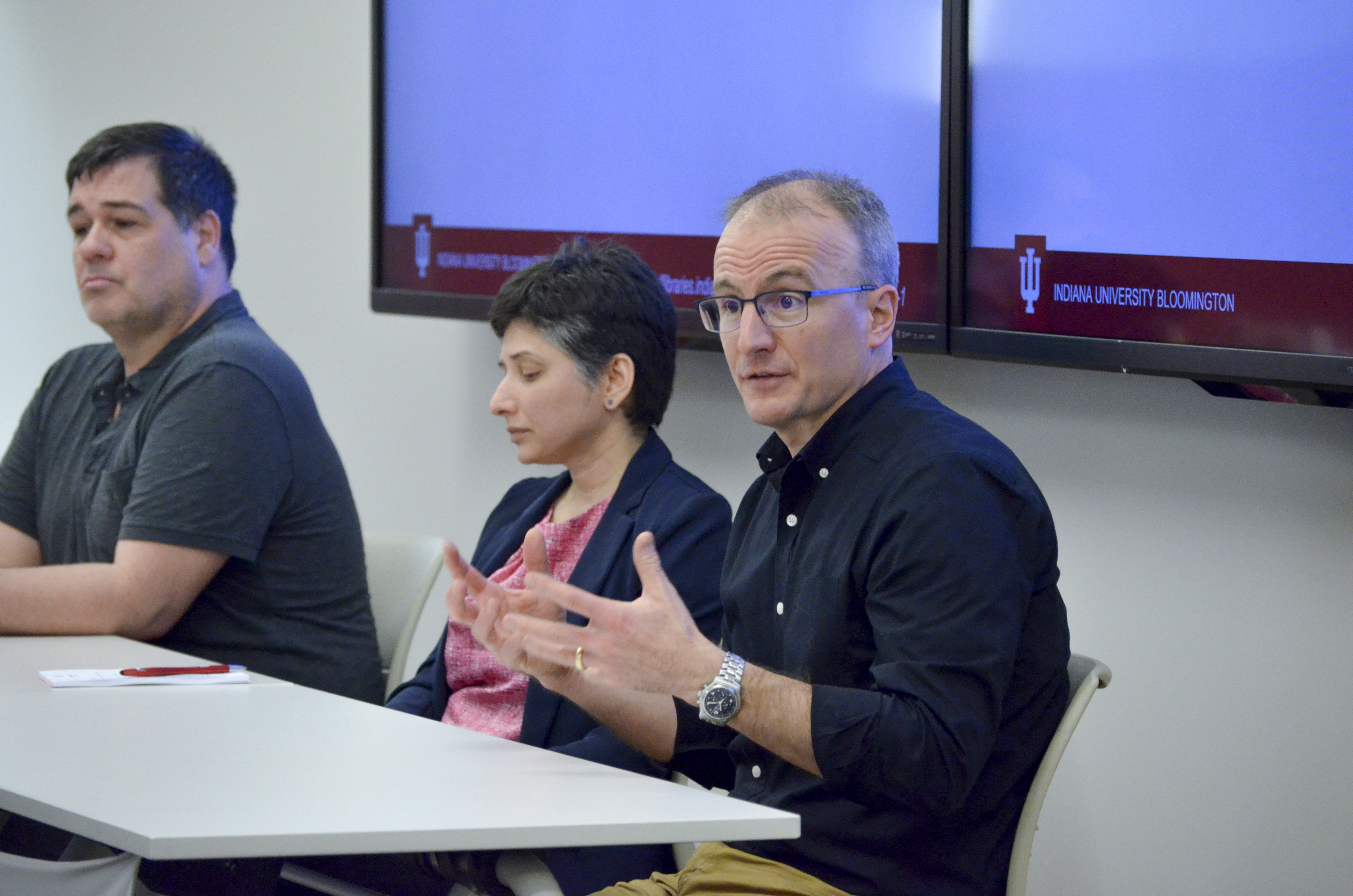 Image of the three fellowship panelists sitting at a table at the front of the room. Rick Hullinger (right) is speaking and gesturing with his hands.