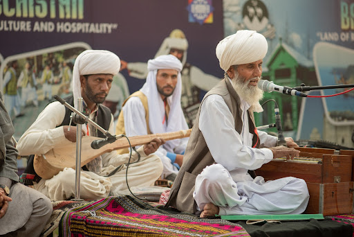 Male Baloch singer playing a harmonium performing with his ensemble sitting next to another male Baloch musician playing a dumbura at the Lok Mela Festival in Islamabad, Pakistan.