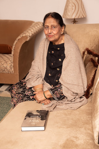 Pakistani singer Suraiyya Multanikar sitting on sofa with a copy of Richard K. Wolf’s book “The Voice in the Drum” on the seat next to her.