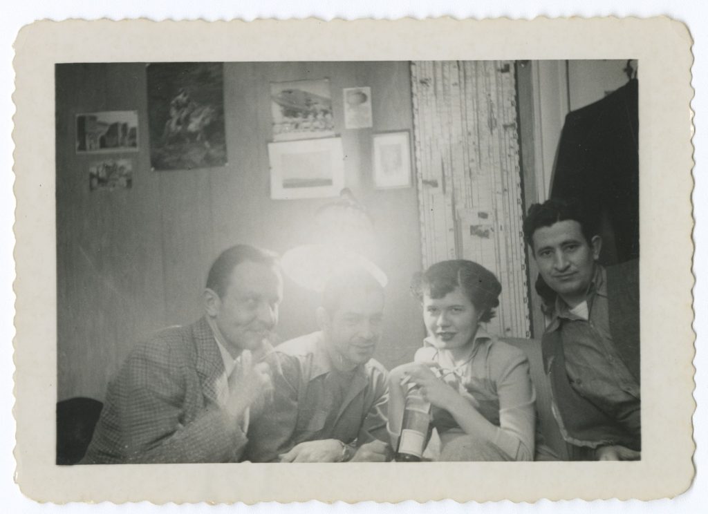 Three unknown men and Barbara Mertz in black and white, sitting under an overexposed lamp and smoking