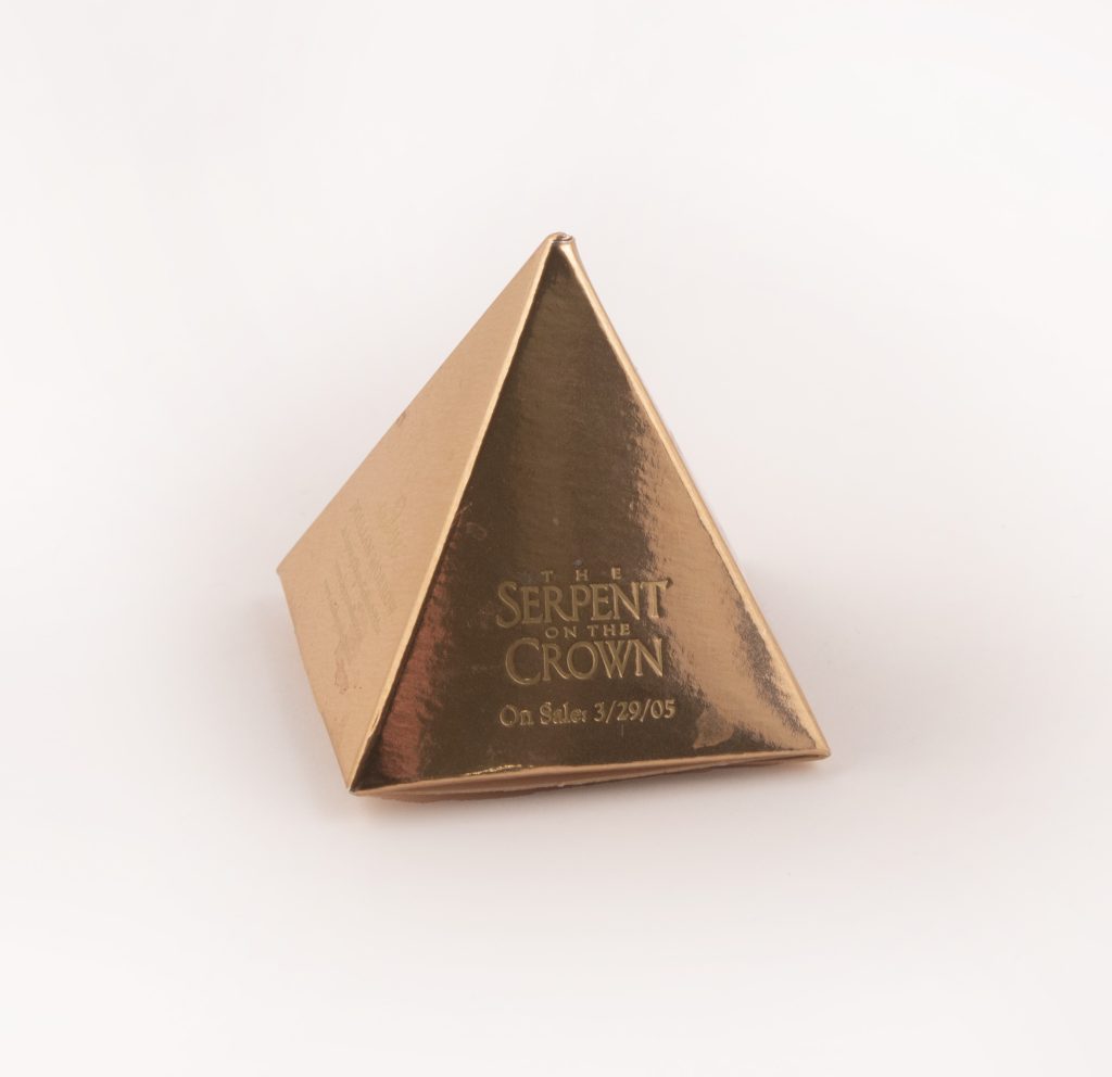 Gold metallic paper pyramid with “The Serpent on the Crown” and “On Sale: 3/29/05” embossed on one side