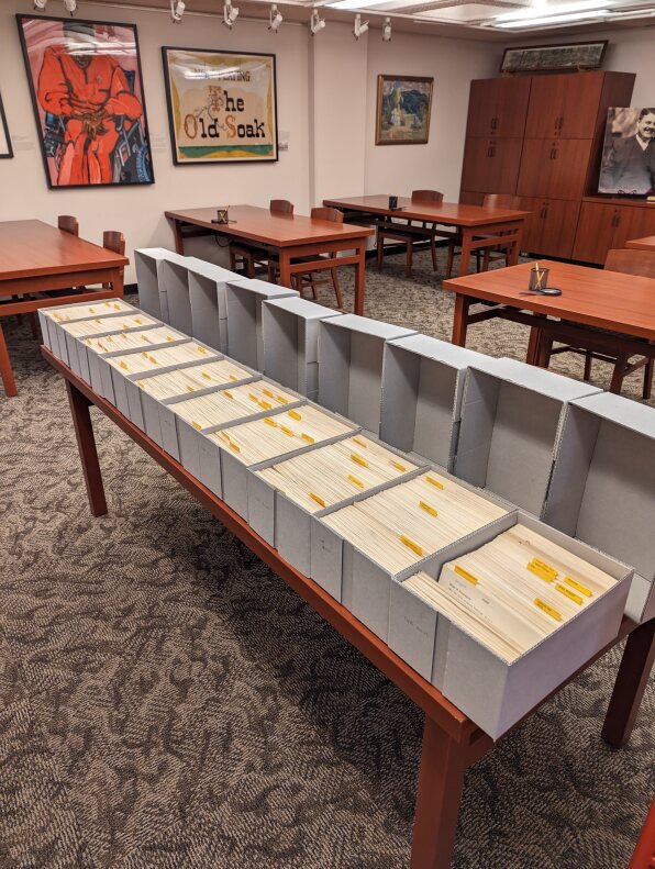 Ten boxes of index cards are placed in a single line on a reading room table at the Indiana University Archives displaying the cards inside.