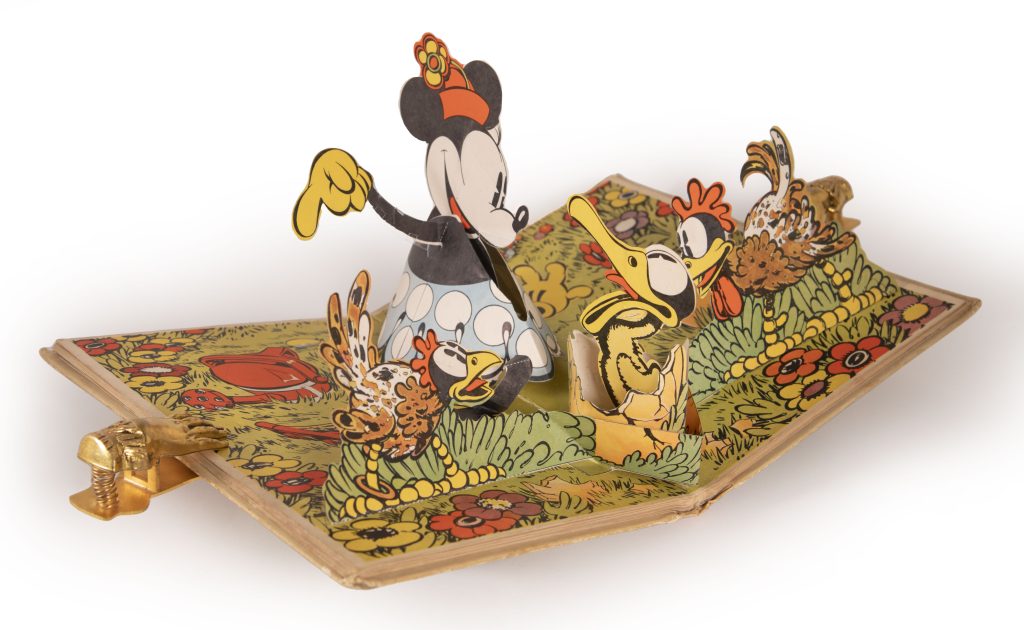 In this Pop-Up image from Pop-Up Minnie Mouse features Minnie standing three dimensionally pointing at the Ugly Duckling, which has just hatched, still sitting in its egg. Two chickens are watching what is happening on both sides of Minnie and the duckling.
